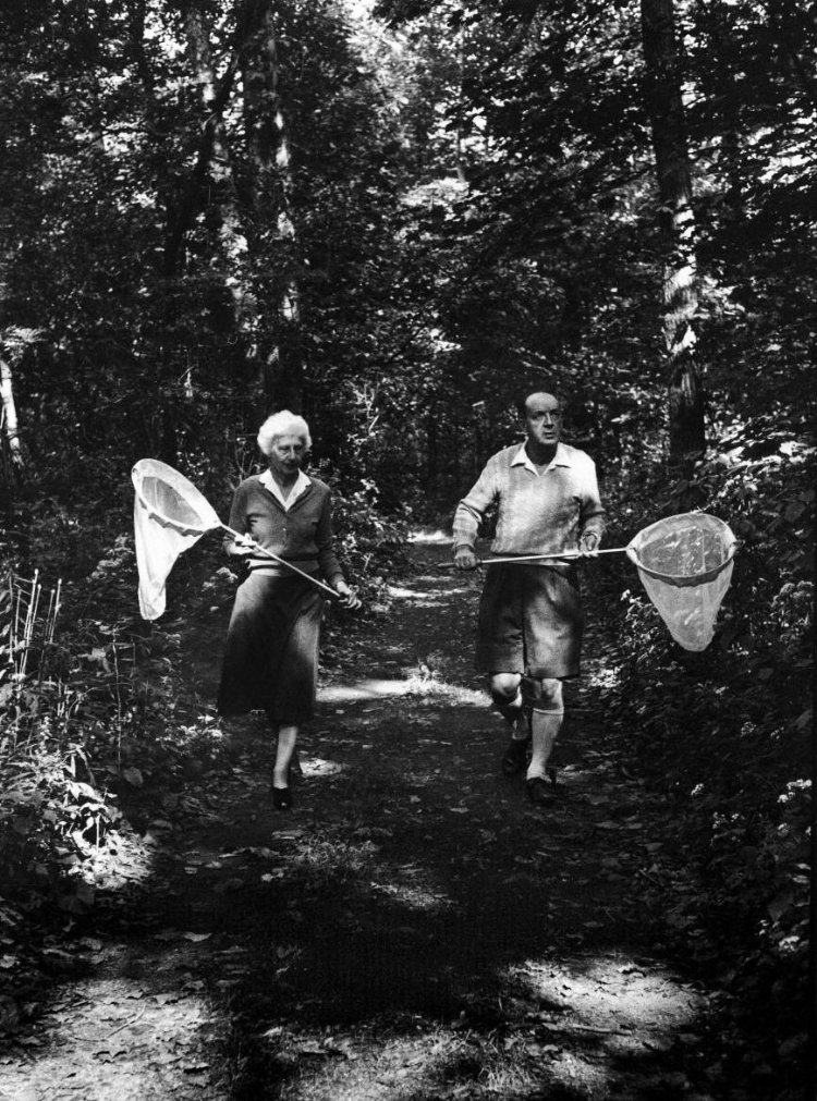 Véra and Vladimir Nabokov alertly perusing a sun-dappled wood, butterfly nets in hand.